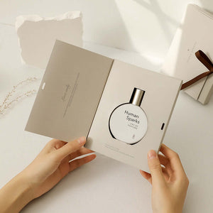 Female hands holding a perfume bottle in an elegant gift box showcasing the Human Sparks fragrance.